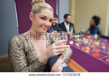 Blonde lifting champagne glass at roulette table in casino