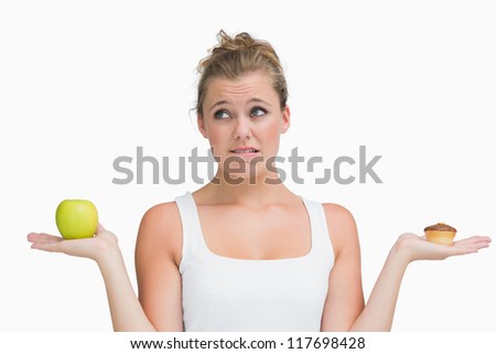 Woman holding apple and cupcake deciding to eat healthily or not