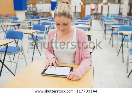Student using tablet pc sitting in empty exam hall in college