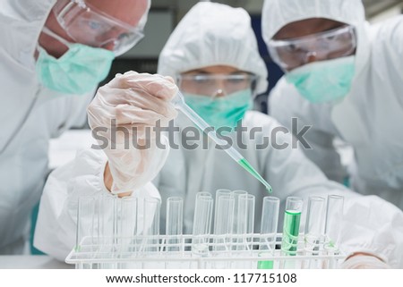 Chemist adding green liquid to test tubes as two others are watching in the lab