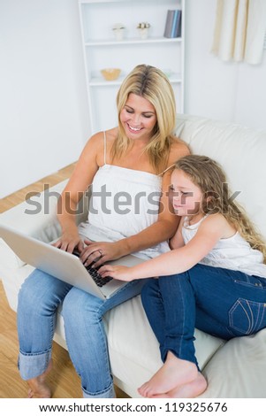 Smiling daughter and mother relaxing on the couch with notebook