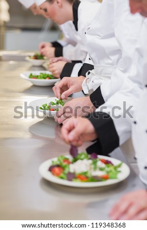 Concentrated Chef\'s team garnishing salads in the kitchen