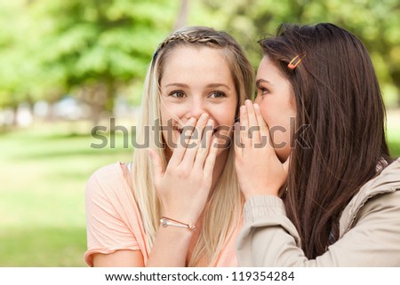 Close-up of teenagers sharing a secret with hands in front of the mouth in a park