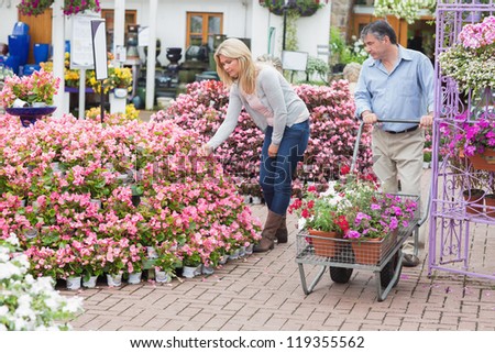 Man pushing the trolley while woman looking at flowers in garden center