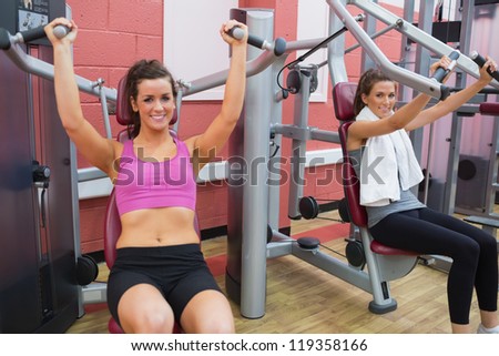 Women using weight machines in gym and smiling