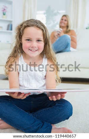 Laughing daughter with a book while her mother is resting on the sofa