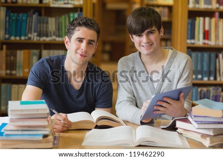 Young men looking up from studying in the library with tablet pc