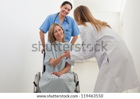 Patient in wheelchair shaking hands with doctor with nurse in hospital corridor