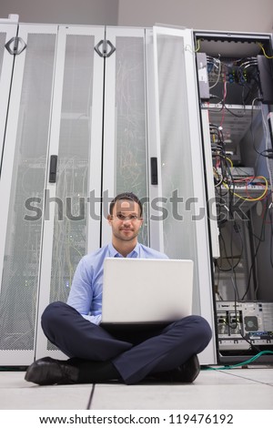Man sitting in front of servers with his laptop on the floor of data center