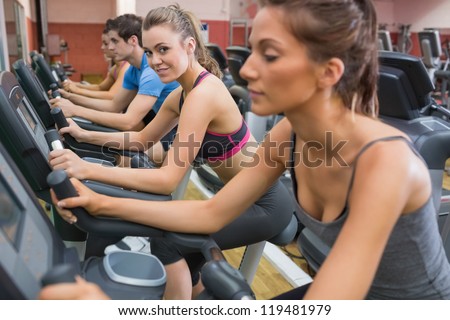 Blonde enjoying exercising on exercise bike in gym with other people