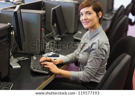 Teacher sitting at the desk while typing at the computer in college computer room