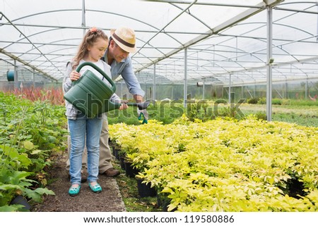 Gardener helping granddaughte watering plants in greenhouse