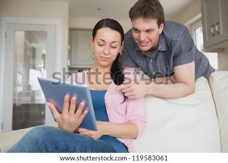 Woman sitting on the couch and uses a tablet computer with her man behind her