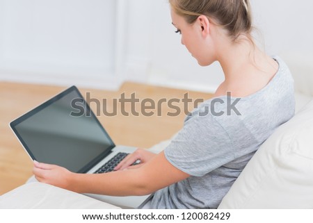 Blonde sitting on the couch in living room and typing on the laptop