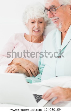 Smiling old couple using laptop in bed