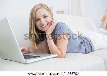 Portrait of casual young woman lying on couch and using laptop at home