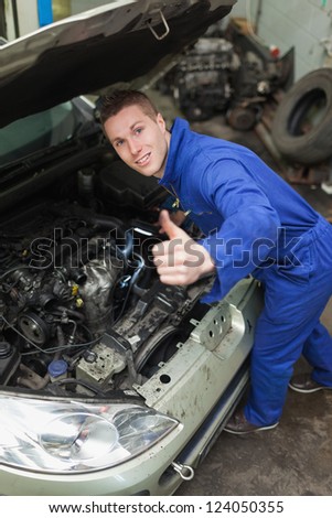 Portrait of auto mechanic by car showing thumbs up sign
