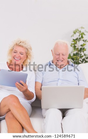 Old couple using a laptop and the tablet on the sofa