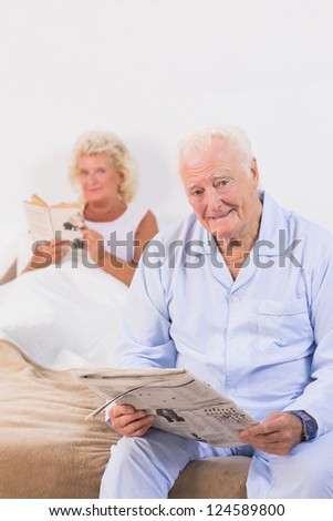 Old persons looking at camera while reading on the bed
