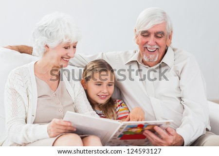 Happy little girl reading with grandparents on the couch
