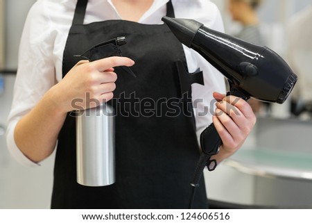 Close-up of female hairdresser holding hair dryer and spray