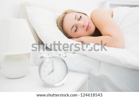 Alarm clock on table with focus on young woman sleeping in bed at home
