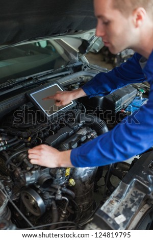 Male mechanic with tablet pc repairing car engine