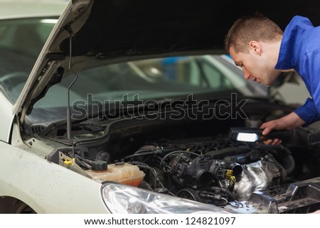 Male mechanic with flashlight examining car engine