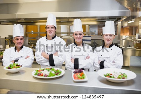 Smiling Chef\'s standing behind salads in the kithcen