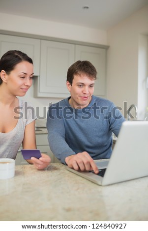 Two people sitting in the kitchen purchasing online on laptop in kitchen