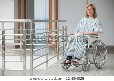 Smiling woman wearing hospital gown sitting in wheelchair in hospital corridor