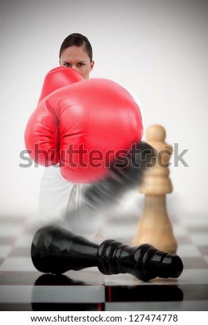 Woman in boxing gloves knocking over chess pieces on chess board