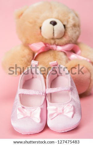 Pink baby booties and teddy bear on pink background