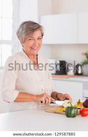Old woman cutting vegetables on a cutting board with a smile in kitchen