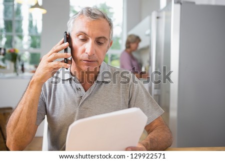 Focused man calling with a sheet of paper while his wife cooking in the kitchen