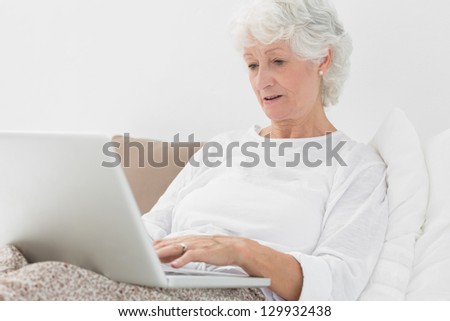 Old woman typing on her laptop lying on her bed