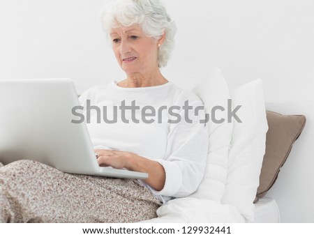 Elderly woman typing on her laptop on the bed
