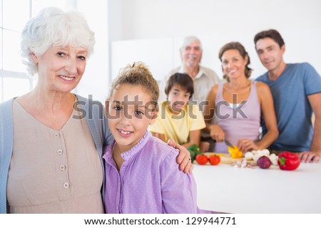 Grandmother and granddaughter standing beside counter with family behind them