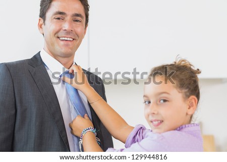 Smiling daughter fixing father tie in kitchen before work