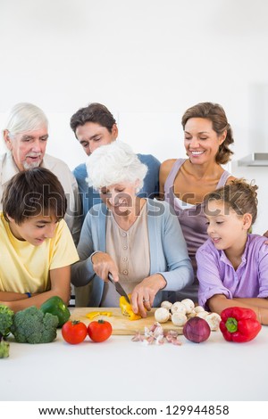 Family watching grandmother slicing pepper in kitchen