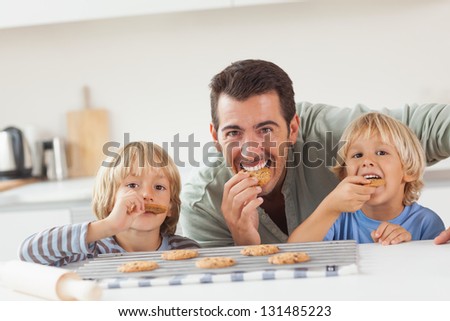 Smiling father and his sons eating cookies in the kitchen