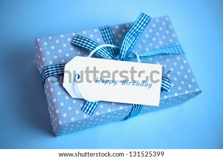 Pretty blue gift with a happy birthday card on a blue background close up