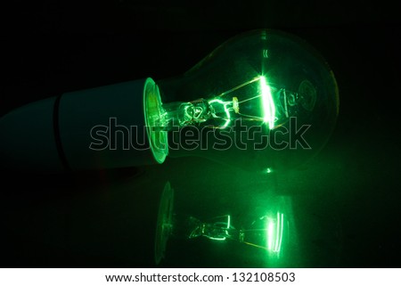Green light bulb turned over on black background on reflective surface