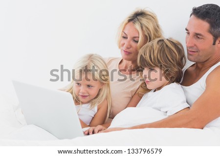 Family watching a laptop screen on a white bed