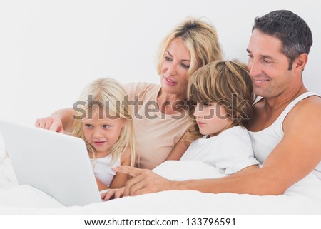 Family watching a laptop screen together on a bed