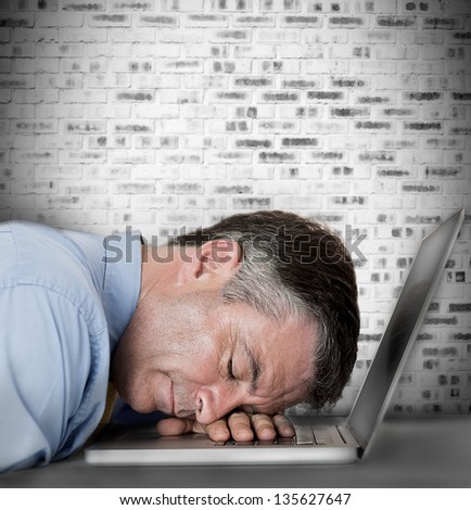 Businessman sleeping on his laptop against grey brick wall