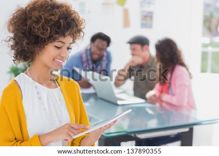 Smiling designer using his tablet pc while team works behind