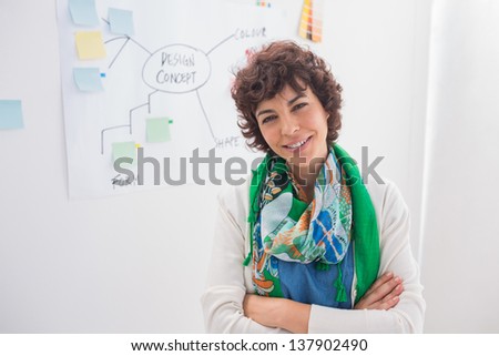Smiling designer with arms folded against white board