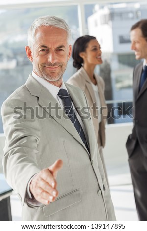 Businessman giving a handshake with colleagues behind discussing together
