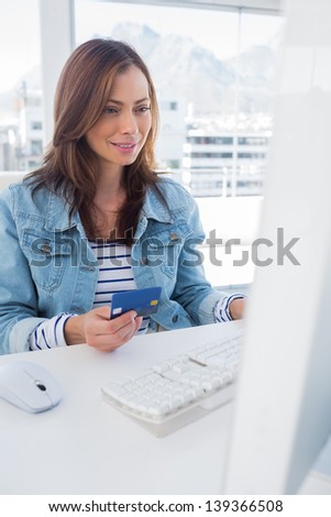 Smiling woman purchasing online with a credit card in a modern bright office
